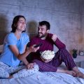 casal na cama assistindo filme e comendo pipoca