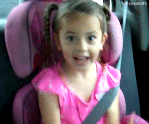 Criança animada no banco de trás de um carro batendo palmas e sorrindo.