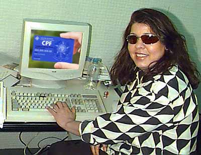 cantora Roberta Miranda sentada de frente a um computador muito antigo e uma mão segurando um CPF está aparecendo na tela, colocada lá por meio de uma montagem