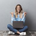 garota sentada no chão com notebook no colo fazendo sinal de positivo com as duas mãos