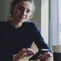 mulher em uma cafeteria usando o celular para criar um perfil no LinkedIn