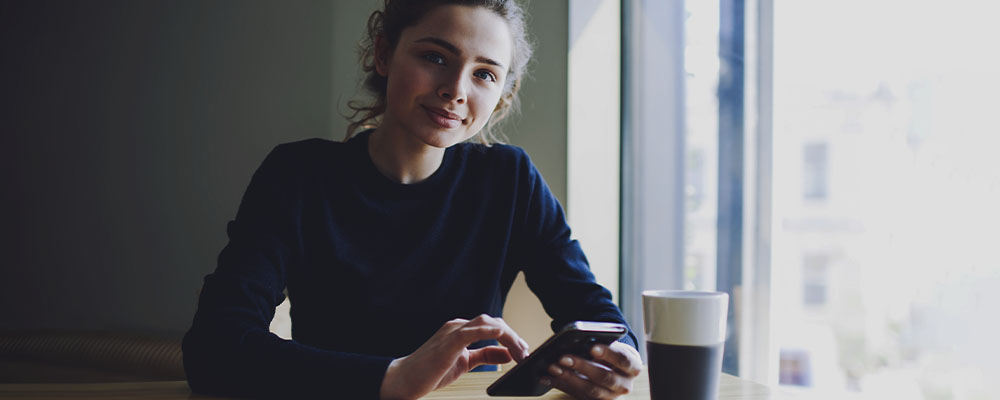 mulher em uma cafeteria usando o celular para criar um perfil no LinkedIn