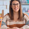 professora sentada na mesa sorrindo na sala de aula