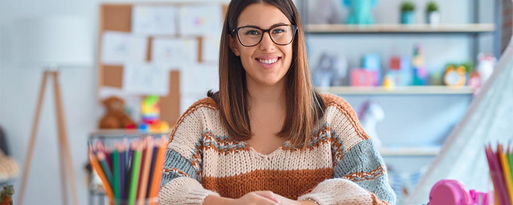 professora sentada na mesa sorrindo na sala de aula