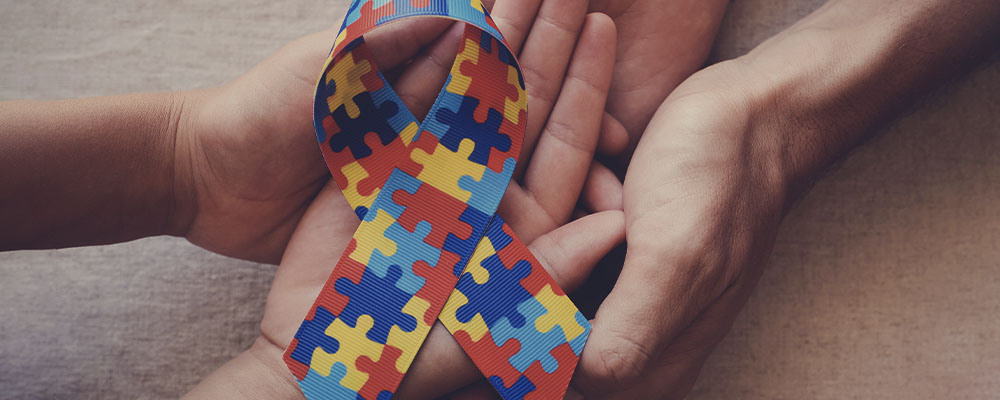 mãos de um adulto entrelaçada com as mãos de uma criança segurando uma faixa colorida símbolo da conscientização sobre o autismo