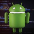 bonequinho do Android em frente à uma tela cheia de códigos
