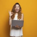 mulher segurando notebook e fazendo sinal de ok com as mãos