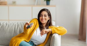 mulher sentada no sofá apontando o controle para a TV enquanto escolhe títulos no catálogo da Netlifx