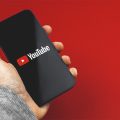 mão segurando um celular com o logo do YouTube aparecendo na tela