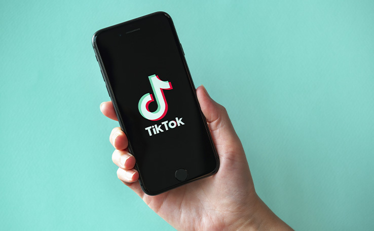 mão segurando um celular com o logo do TikTok aparecendo na tela