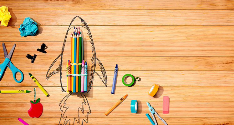 foguete feito com materiais escolares em cima de uma mesa de madeira, simbolizando o estímulo da criatividade