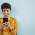 mulher usando celular encostada em uma parede azul