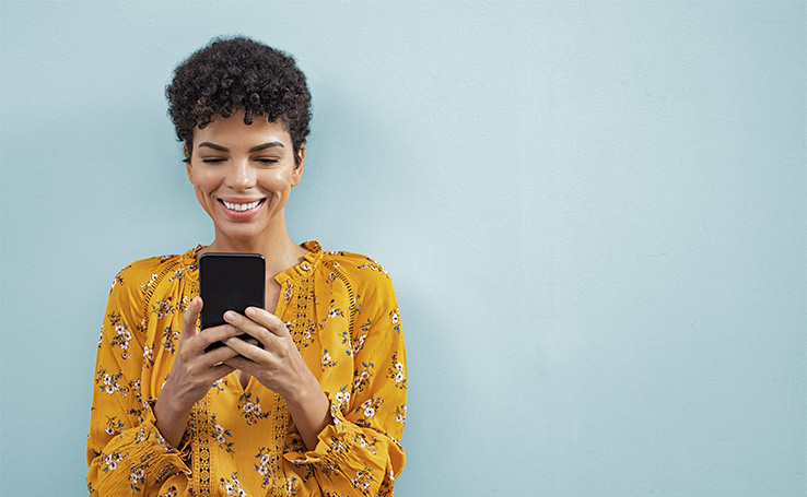 mulher usando celular encostada em uma parede azul