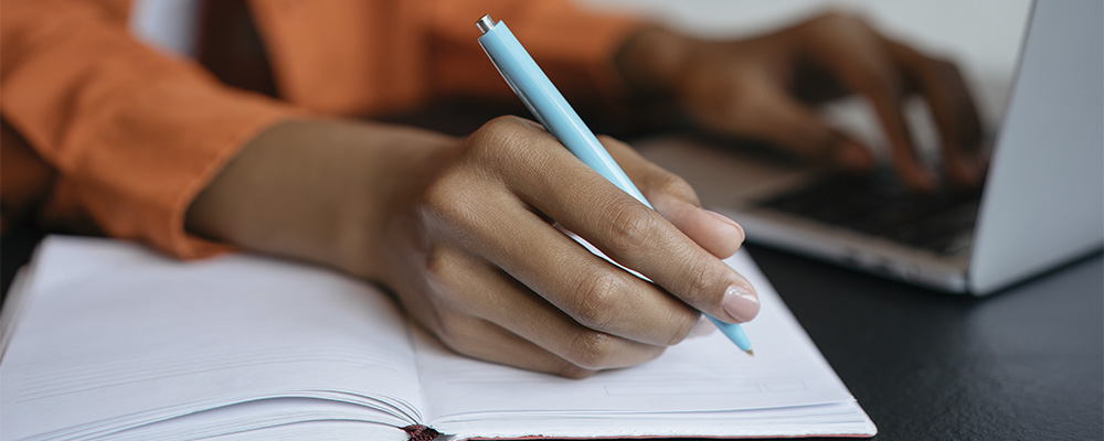 garota estudando pelo computador e escrevendo um resumo à mão