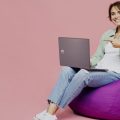 mulher sentada em um poof acessando sites em um notebook da Positivo