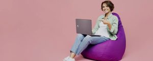 mulher sentada em um poof acessando sites em um notebook da Positivo