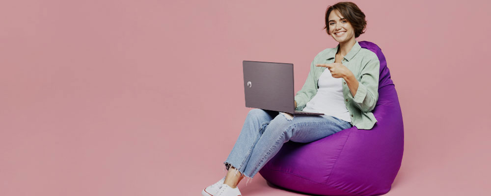 mulher sentada em um poof acessando sites em um notebook da Positivo
