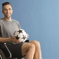 homem na cadeira de rodas segurando uma bola de futebol inclusivo