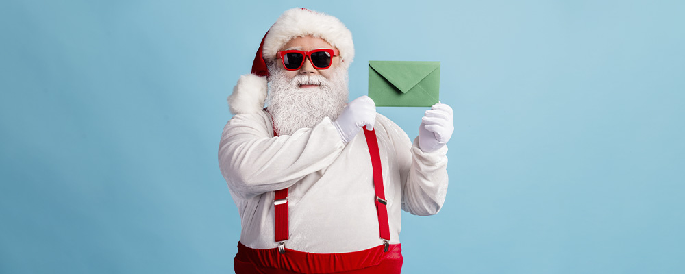 Papai Noel de óculos escuros segurando uma cartinha
