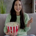 mulher sentada no sofá comendo pipoca e assistindo aos lançamentos da Netflix