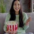 mulher sentada no sofá comendo pipoca e assistindo aos lançamentos da Netflix