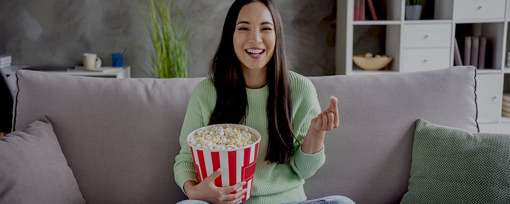 mulher sentada no sofá comendo pipoca e assistindo aos lançamentos da Netflix