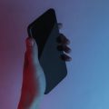 pessoa segurando o celular em um ambiente escuro sobre um fundo degradê de rosa com azul