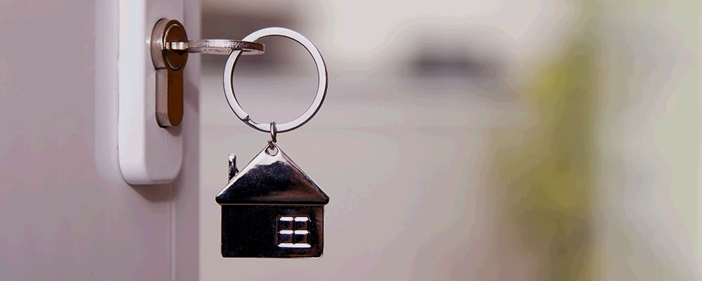 chave na fechadura de uma porta adornada com um chaveiro em formato de casa, fazendo alusão a casas de aluguel para férias, que podem ser encontradas no Booking