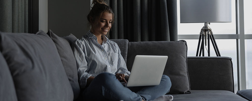 mulher sorrindo enquanto usa o WhatsApp em um notebook no sofá da sala