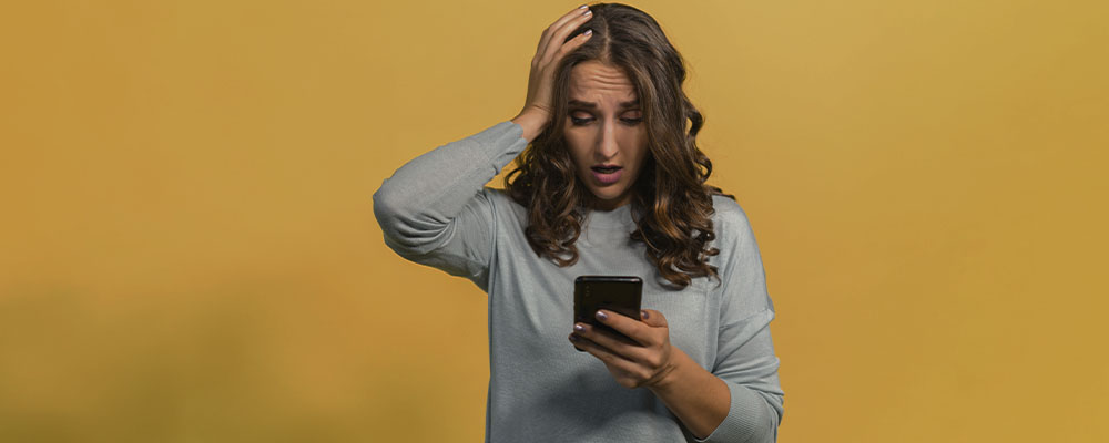 mulher com a mão na cabeça olhando preocupada para a tela do celular