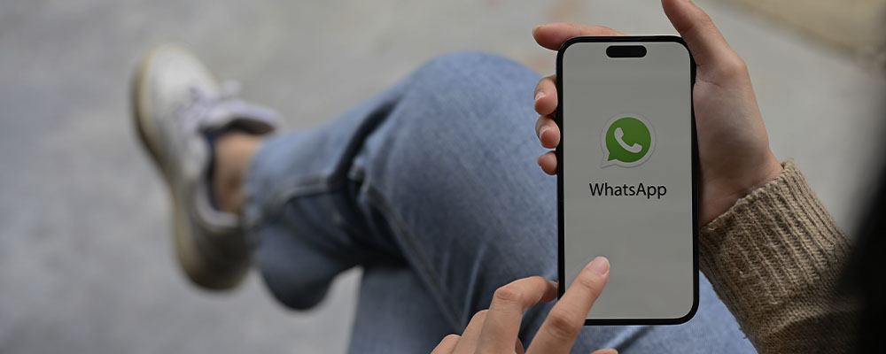 mulher sentada de pernas cruzadas com o WhatsApp aberto no celular