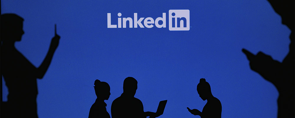 sombras de pessoas mexendo em celulares e notebooks com o logo do LinkedIn acima delas em um fundo azul