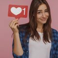 garota segurando uma plaquinha com símbolo de coração e o número 1 ao lado, representando os likes de redes sociais