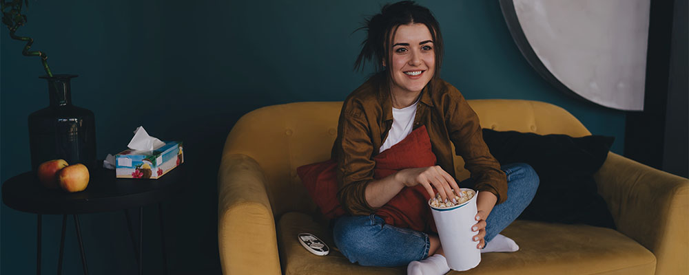 mulher sentada no sofá comendo pipoca e assistindo os lançamentos da Netflix