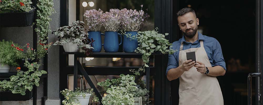 microempresário na porta de sua floricultura consultando dados de sua MEI pelo celular