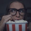 mulher com o olhar intrigado atrás de um balde de pipoca porque está assistindo filmes de suspense