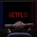 homem sentado com as mãos atrás da cabeça assistindo Netflix na televisão