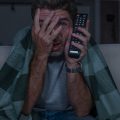 homem com muito medo enrolado na coberta assisitindo filmes de terror