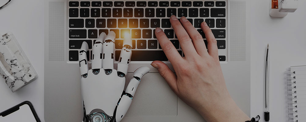 mão de um robô ao lado da mão de uma mulher digitando no teclado de um computador