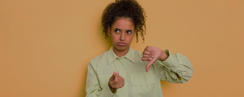 mulher com cara triste fazendo sinal de dinheiro com uma mão e apontando o polegar para baixo com a outra mão mostrando que não tem dinheiro