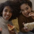 duas amigas comendo pipoca e pizza enquanto assistem os lançamentos da Netflix