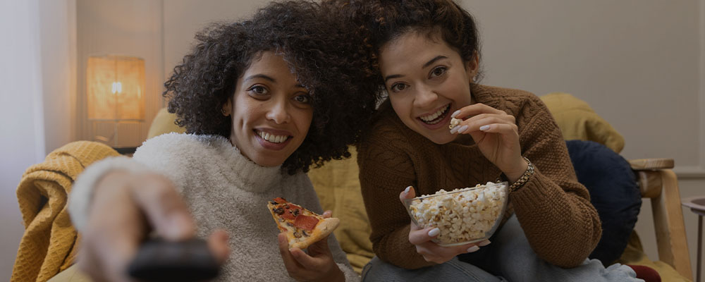 duas amigas comendo pipoca e pizza enquanto assistem os lançamentos da Netflix
