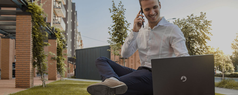 homem fazendo uma ligação enquanto usa um notebook da Positivo para trabalhar ao ar livre