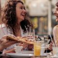 Amigas sorrindo enquanto comem pizza no exterior de um restaurante.