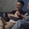 Casal assistindo séries da Netflix sentados em um sofá comendo pipoca.
