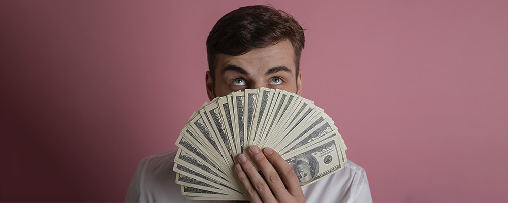 Homem cobrindo o rosto com várias notas de dinheiro em formato de leque.
