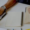 Dupla de amigos fazendo trabalho da faculdade com livros e um notebook.