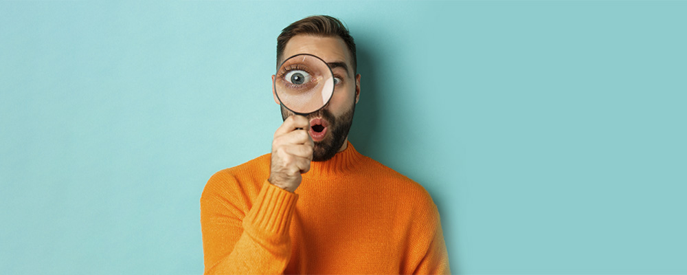 Homem segurando uma lupa sobre o rosto representando a busca por imagem na Shopee, Shein e Ali Express.