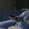 Mulher no sofá comendo pipoca enquanto assiste Netflix.
