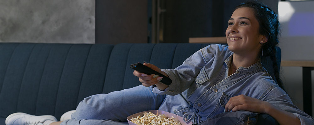 Mulher no sofá comendo pipoca enquanto assiste Netflix.